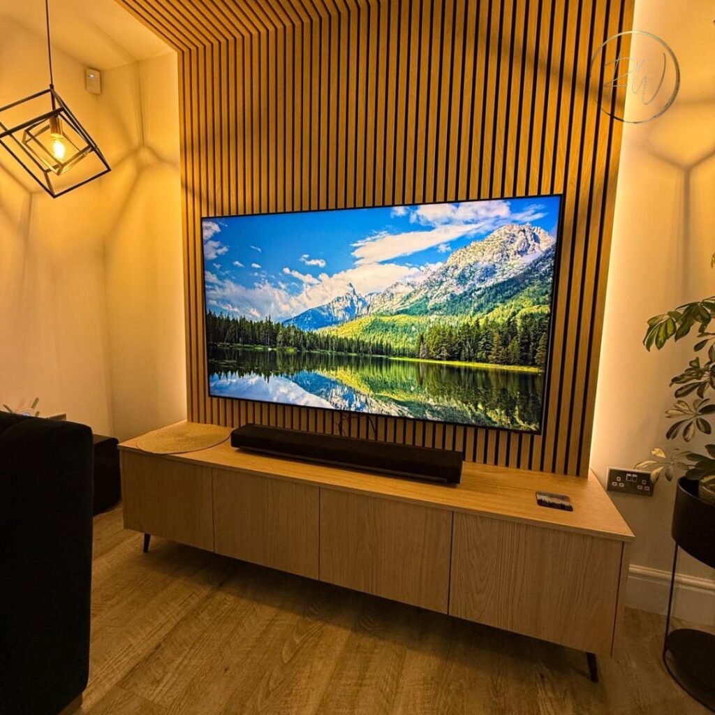 Bespoke oak media wall with slatted timber panelling, floating media unit, feature lighting and a wall-mounted television.