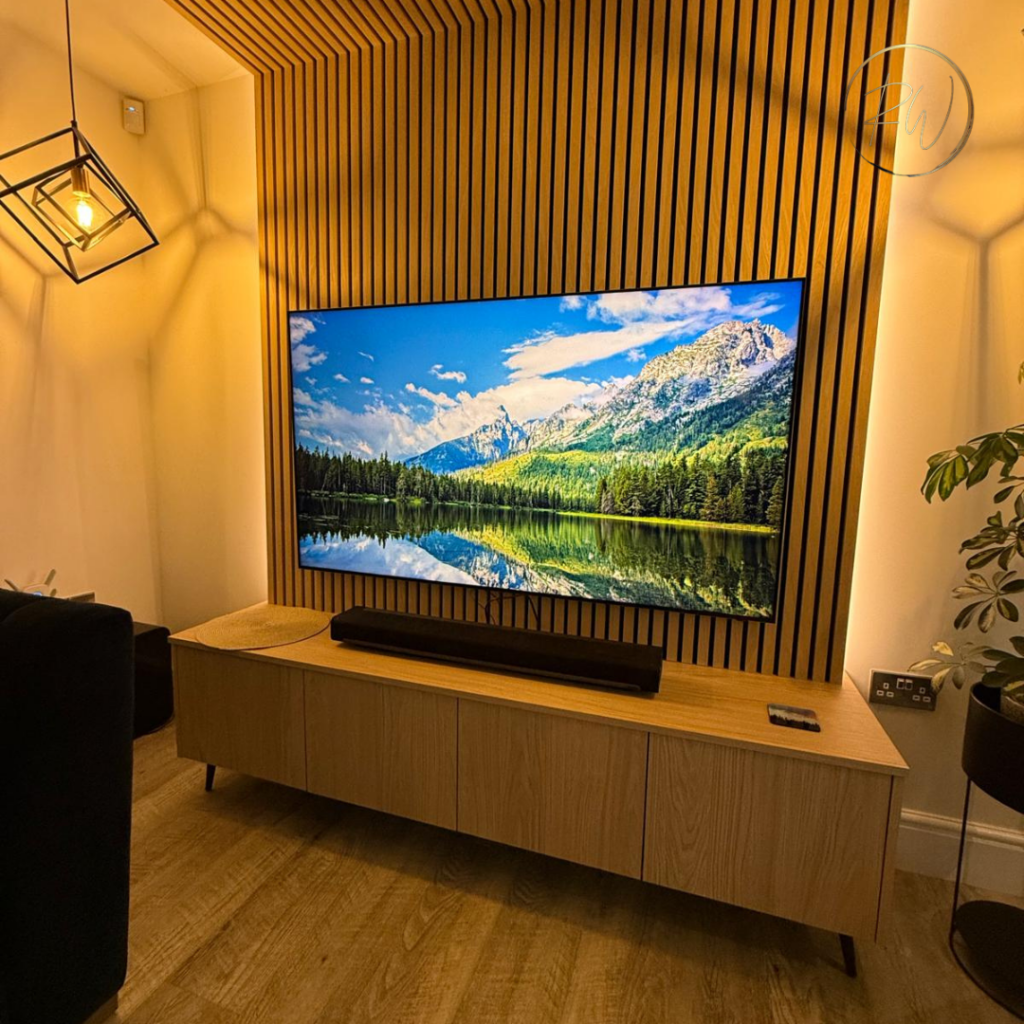 Bespoke oak media wall with wall-mounted television, vertical acoustic slatted panelling, integrated lighting and floating storage unit in Broadstone.