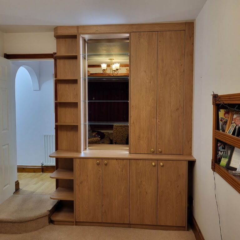 Bespoke fitted bedroom furniture with integrated wardrobe, shelving, drawers and display cabinet in an oak finish.