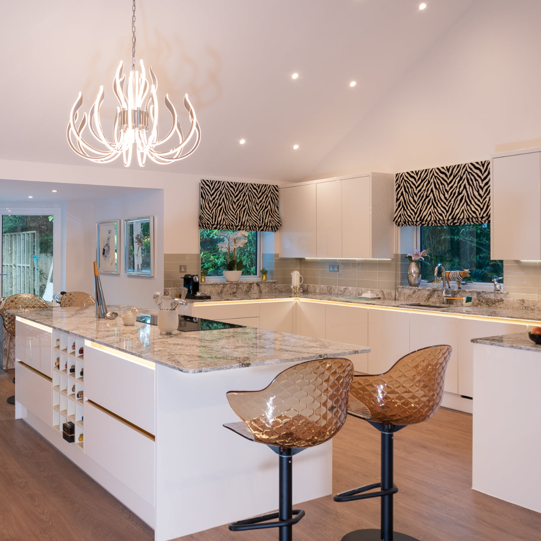 Contemporary open-plan kitchen transformation featuring white handleless cabinetry, a large marble-effect island with breakfast bar, integrated wine storage, feature pendant lighting and stone-effect worktops.