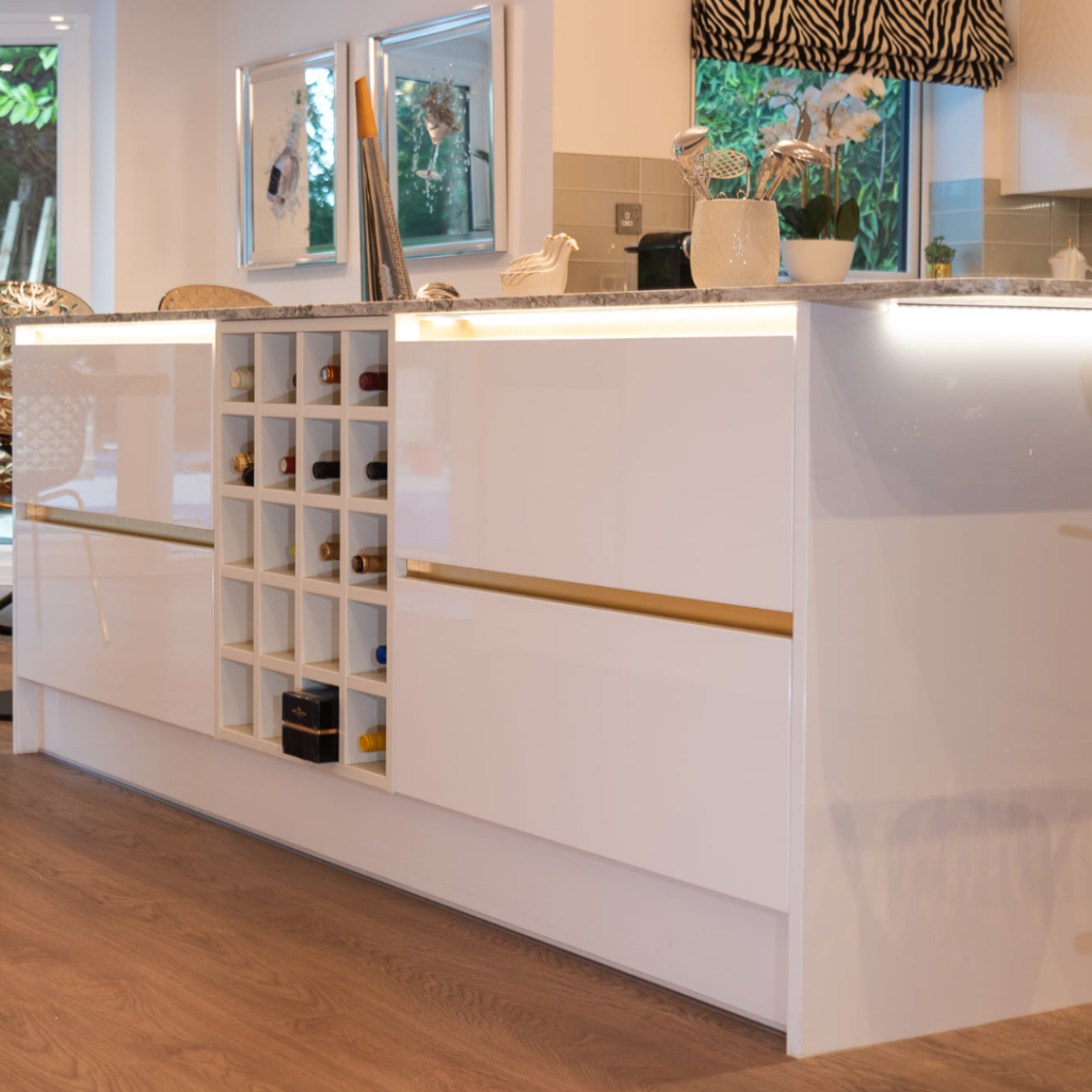 Close-up of a contemporary kitchen island with white handleless cabinetry, integrated wine storage, stone-effect worktops and concealed LED lighting.