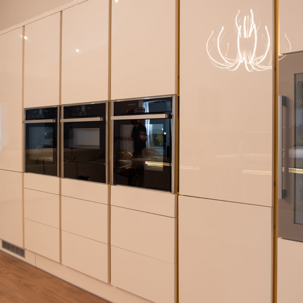 Full-height white handleless kitchen cabinetry with integrated double ovens, concealed storage and a sleek contemporary finish.