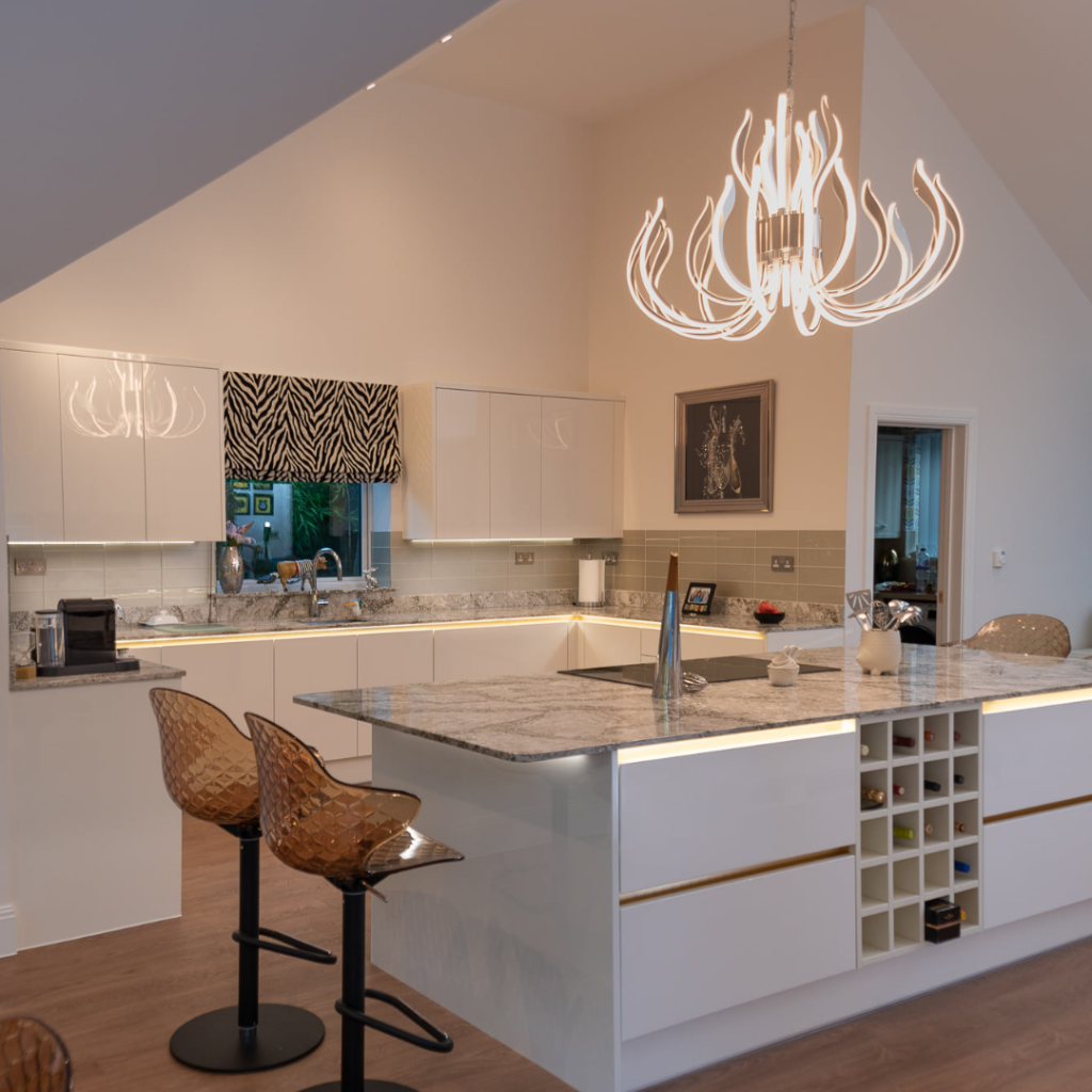 Contemporary open-plan kitchen with a large island, white handleless cabinetry, stone-effect worktops, integrated wine storage and feature pendant lighting.