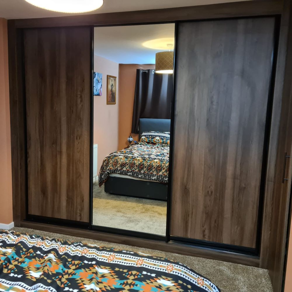 Bespoke sliding wardrobe installation featuring dark wood-effect doors, a mirrored panel and space-saving fitted bedroom storage.