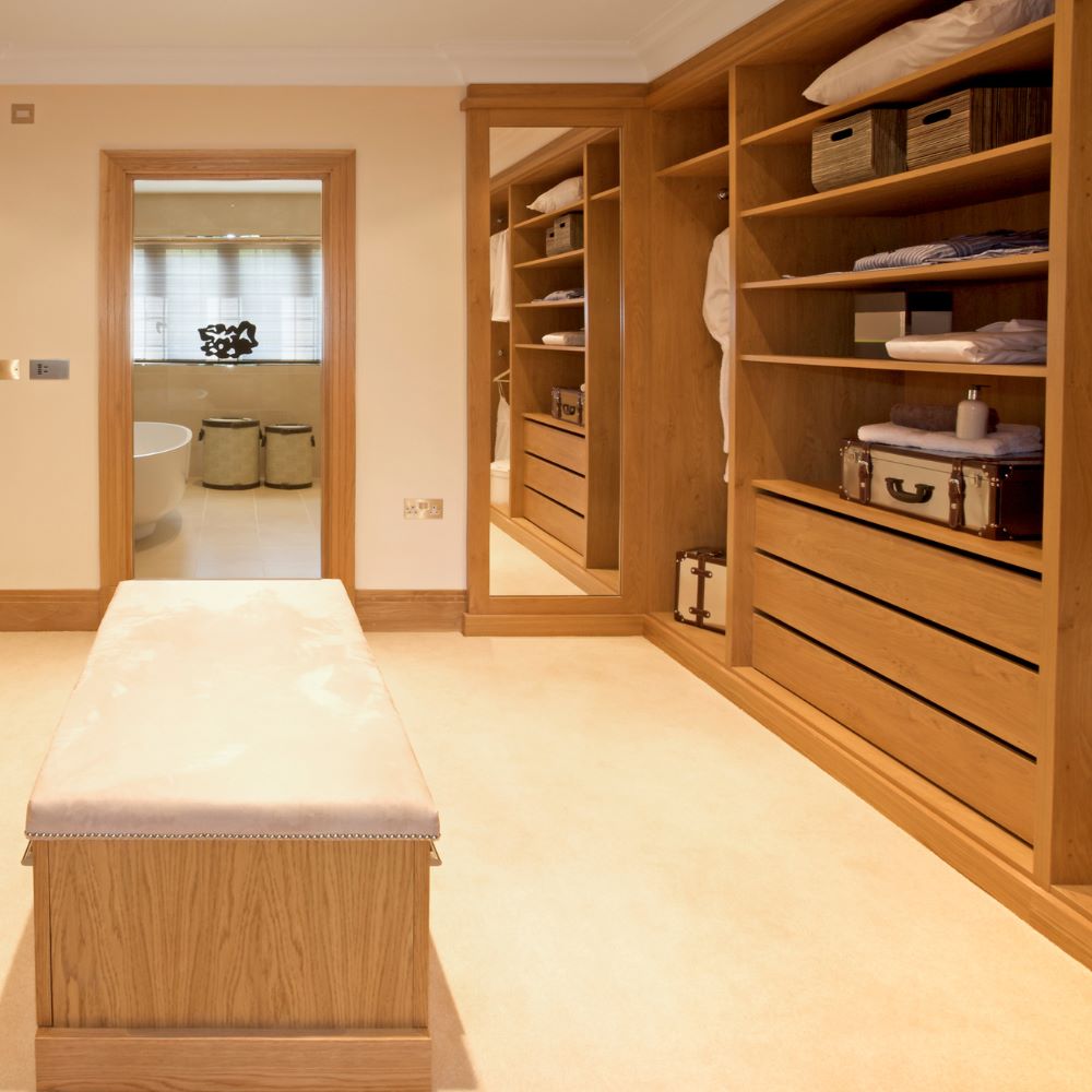 Bespoke walk-in wardrobe with oak-effect fitted storage, integrated drawers, open shelving, hanging rails and a full-length mirror.