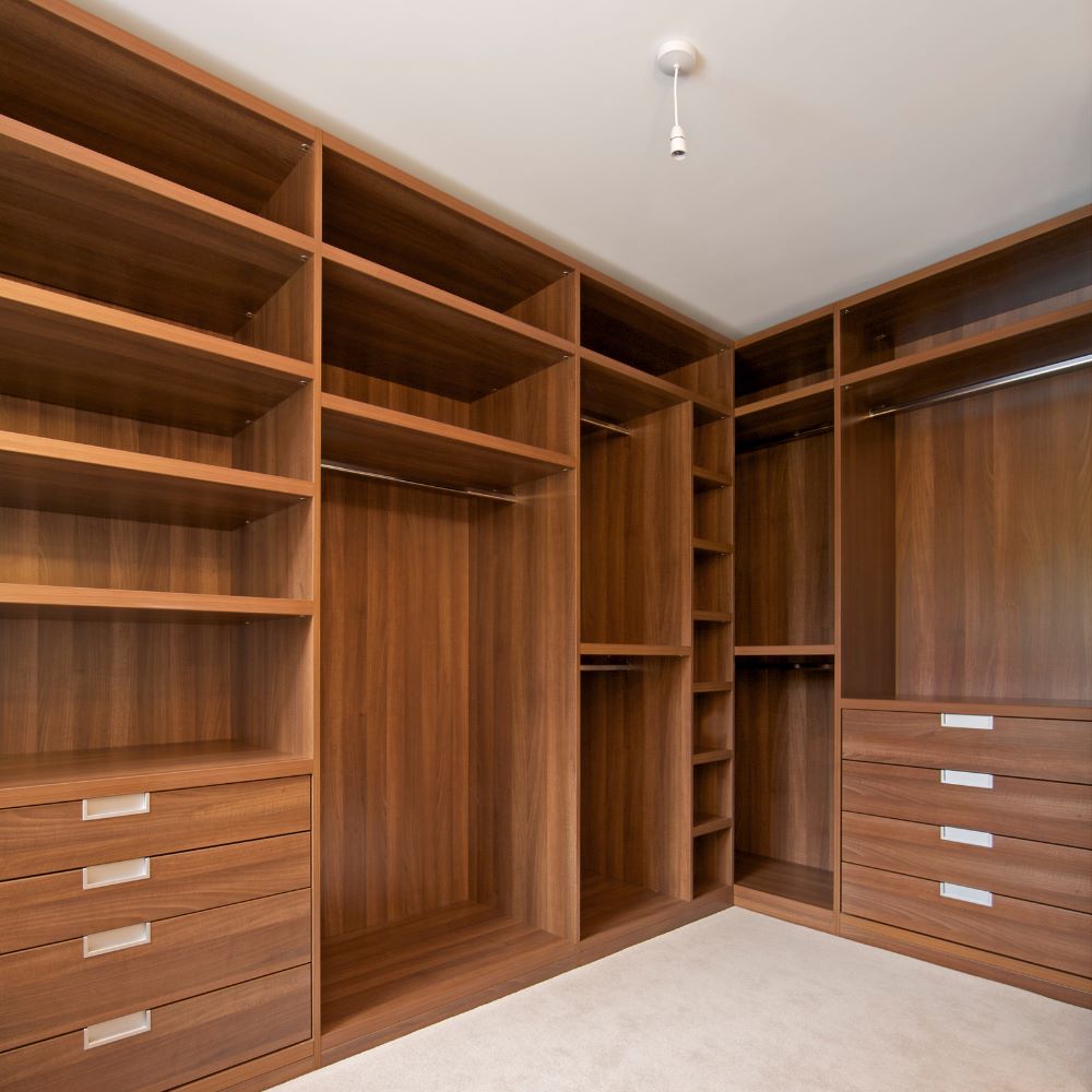 Bespoke walk-in wardrobe with walnut-effect fitted shelving, hanging rails, integrated drawers and custom storage compartments.
